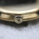 Close-up of the gold-toned crown with the Mondaine 'M' logo.