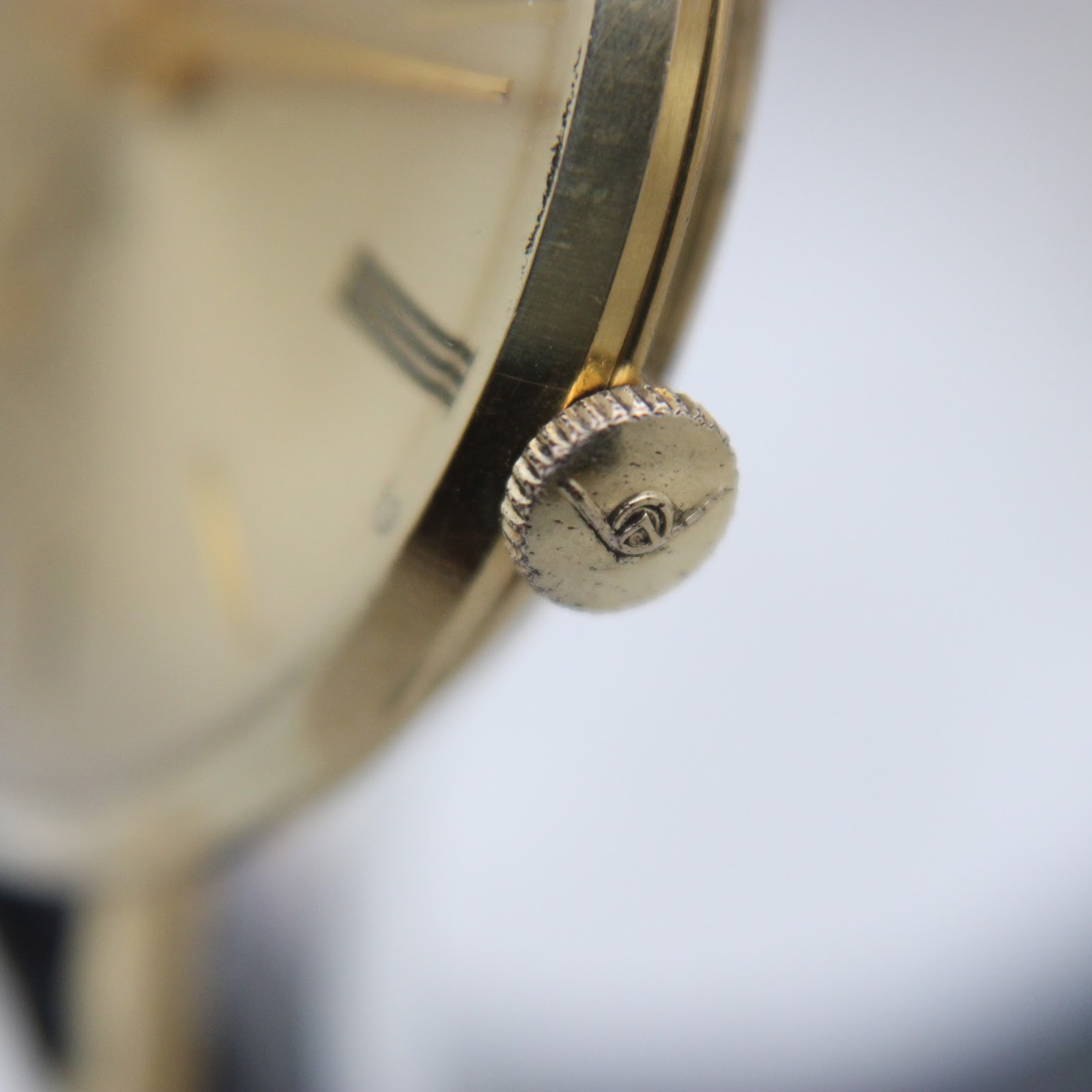 Close-up side view of the signed gold-toned crown on the Mondaine watch.