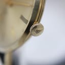 Close-up side view of the signed gold-toned crown on the Mondaine watch.