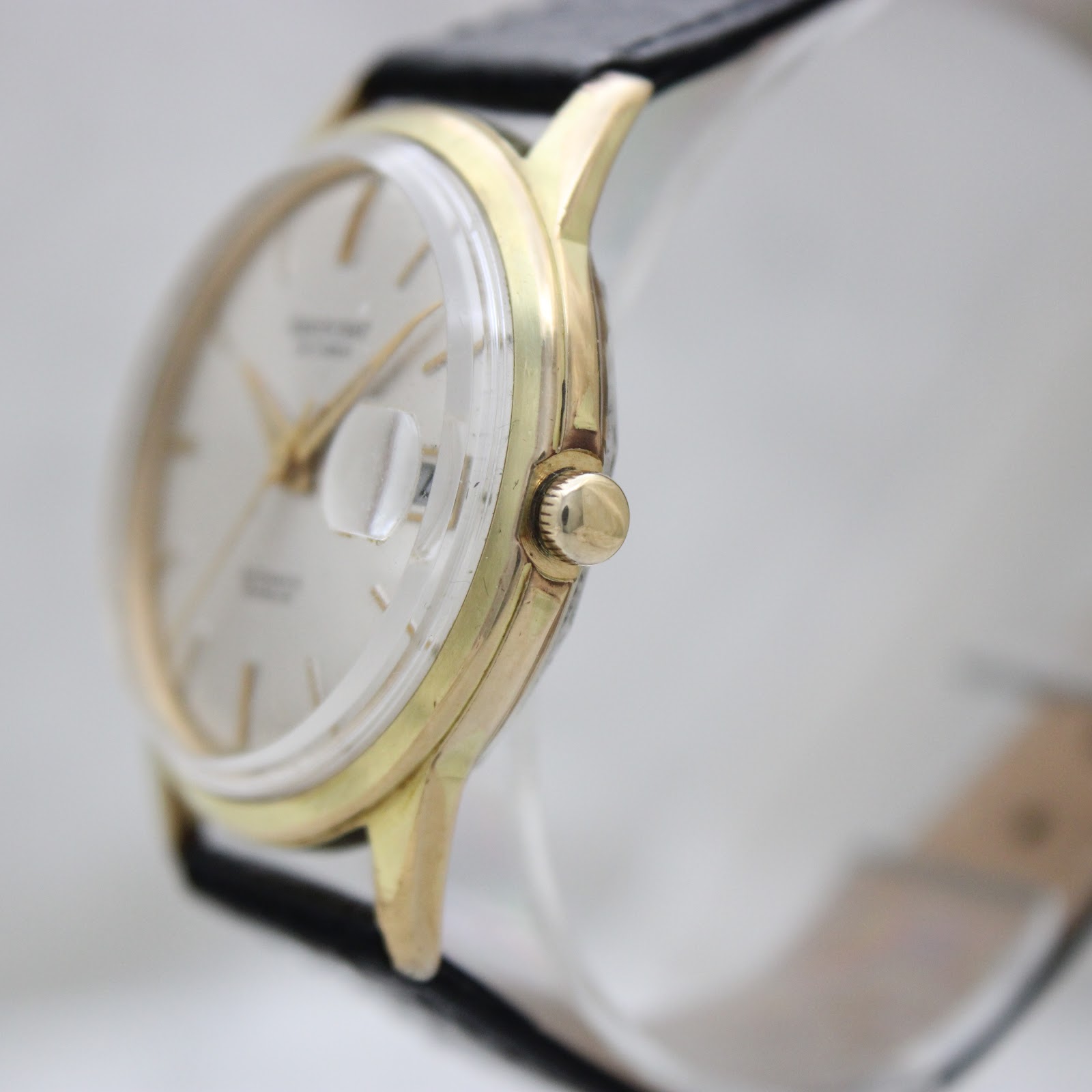 Side view of the Aristocrat watch showing the unsigned crown and gold-tone case on a display stand.