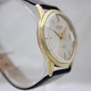 Angled side view of the Aristocrat watch case, highlighting the gold-tone finish and acrylic crystal.