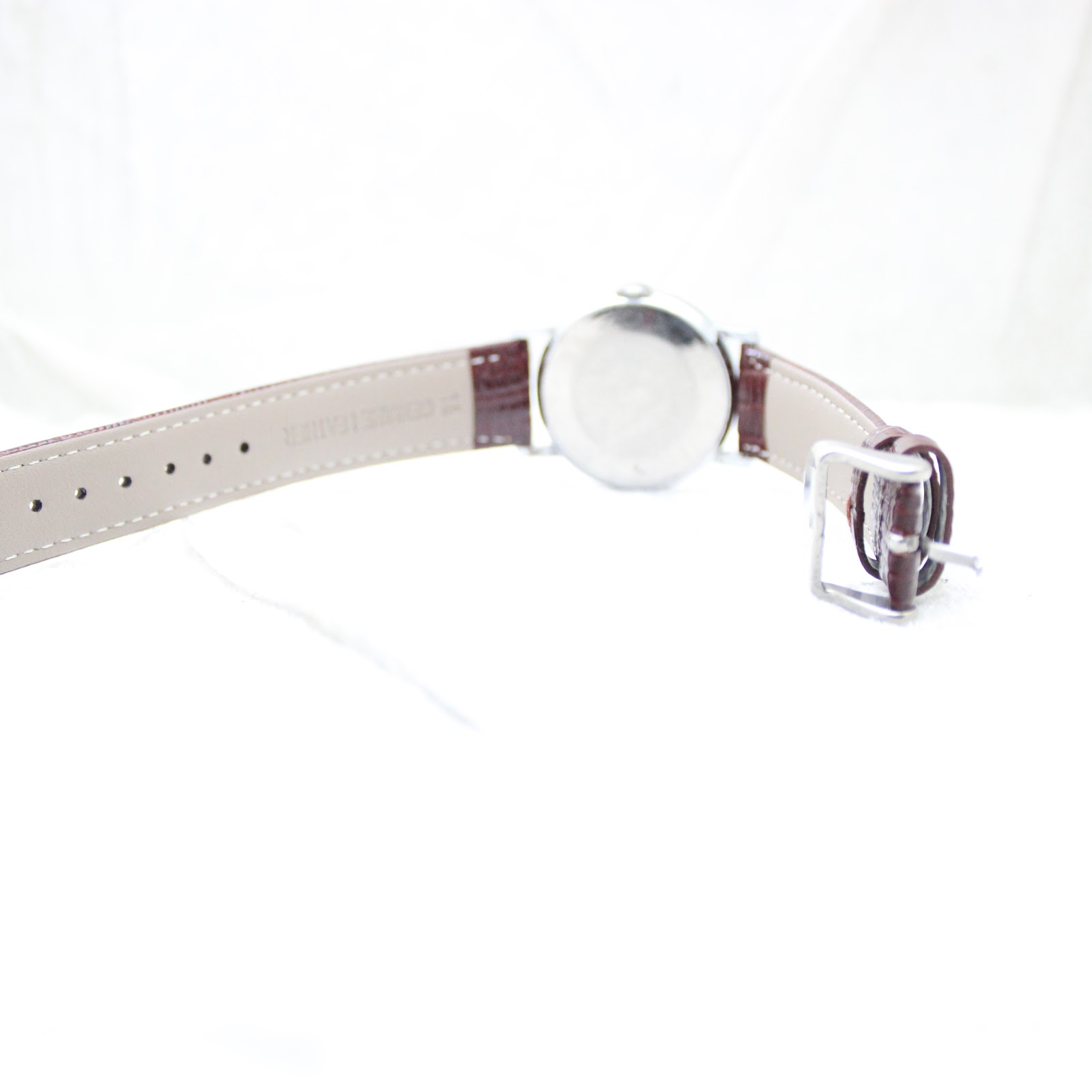 View of the watch from the underside, showing the reverse of the burgundy brown leather strap and pin buckle.