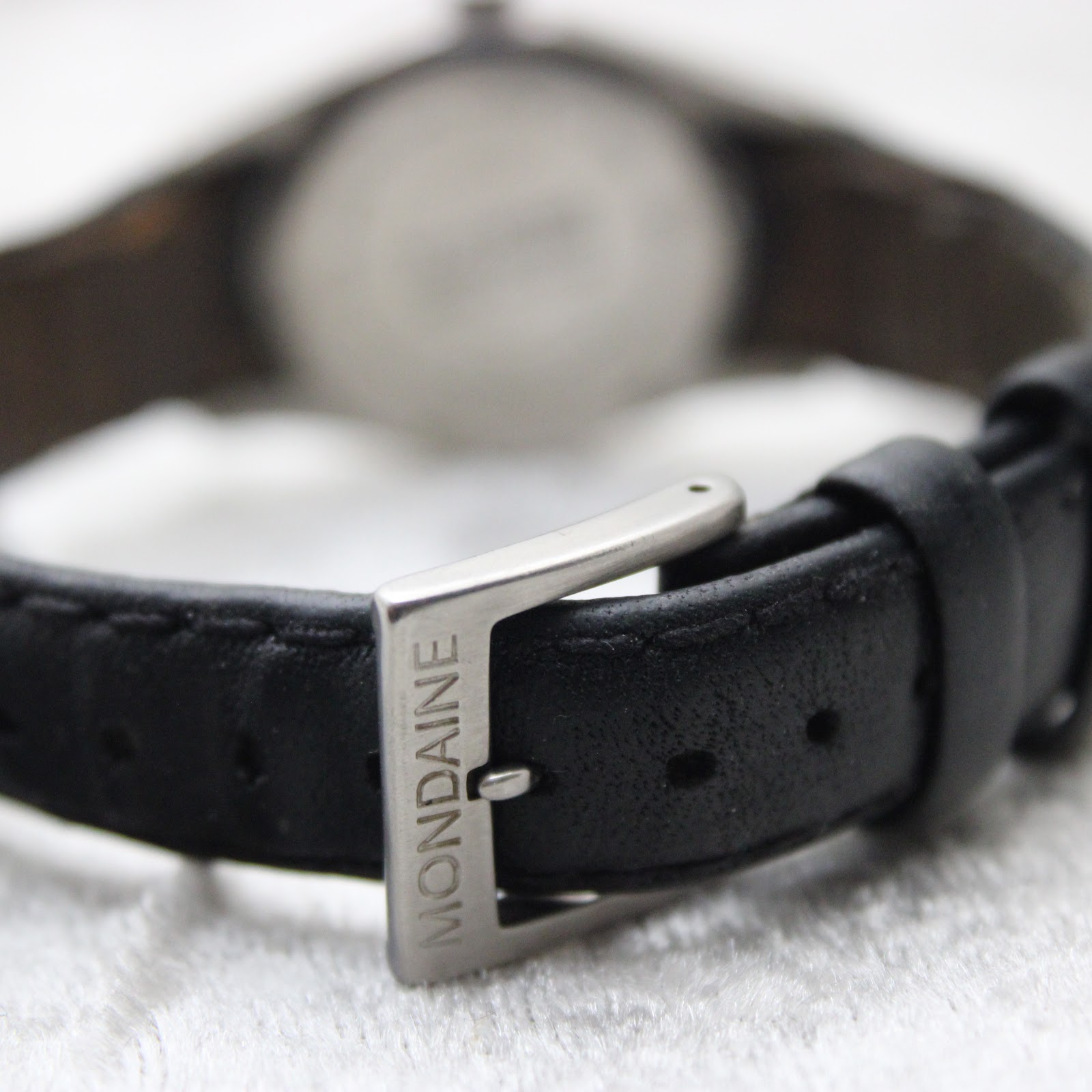 Close-up of the stainless steel buckle on the black leather strap, signed "MONDAINE"