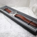 The watch presented inside a black display box, highlighting its full length and brown leather strap.