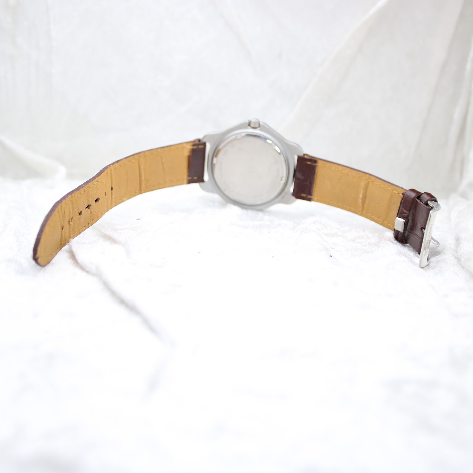 Rear view of the watch showing the stainless steel caseback and the brown leather strap laid open.
