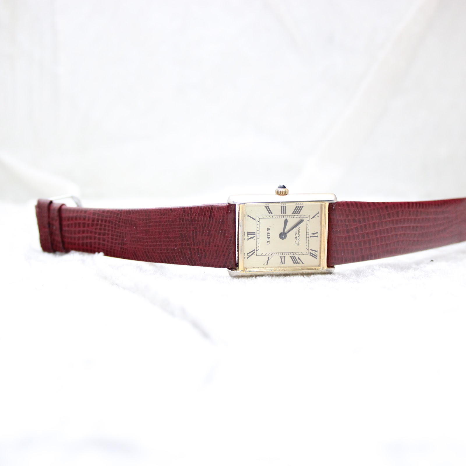 Full front view of the Corteal watch lying flat on a white surface, showcasing the gold-tone dial and burgundy strap.
