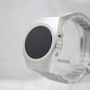 Angled side view of the silver-tone LED digital watch on a clear stand, showing the push-button on the right side of the case.