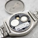 Interior view of the watch movement with the case back removed, showing two AG12 button cell batteries and a "US components assembled in Malaysia" sticker.