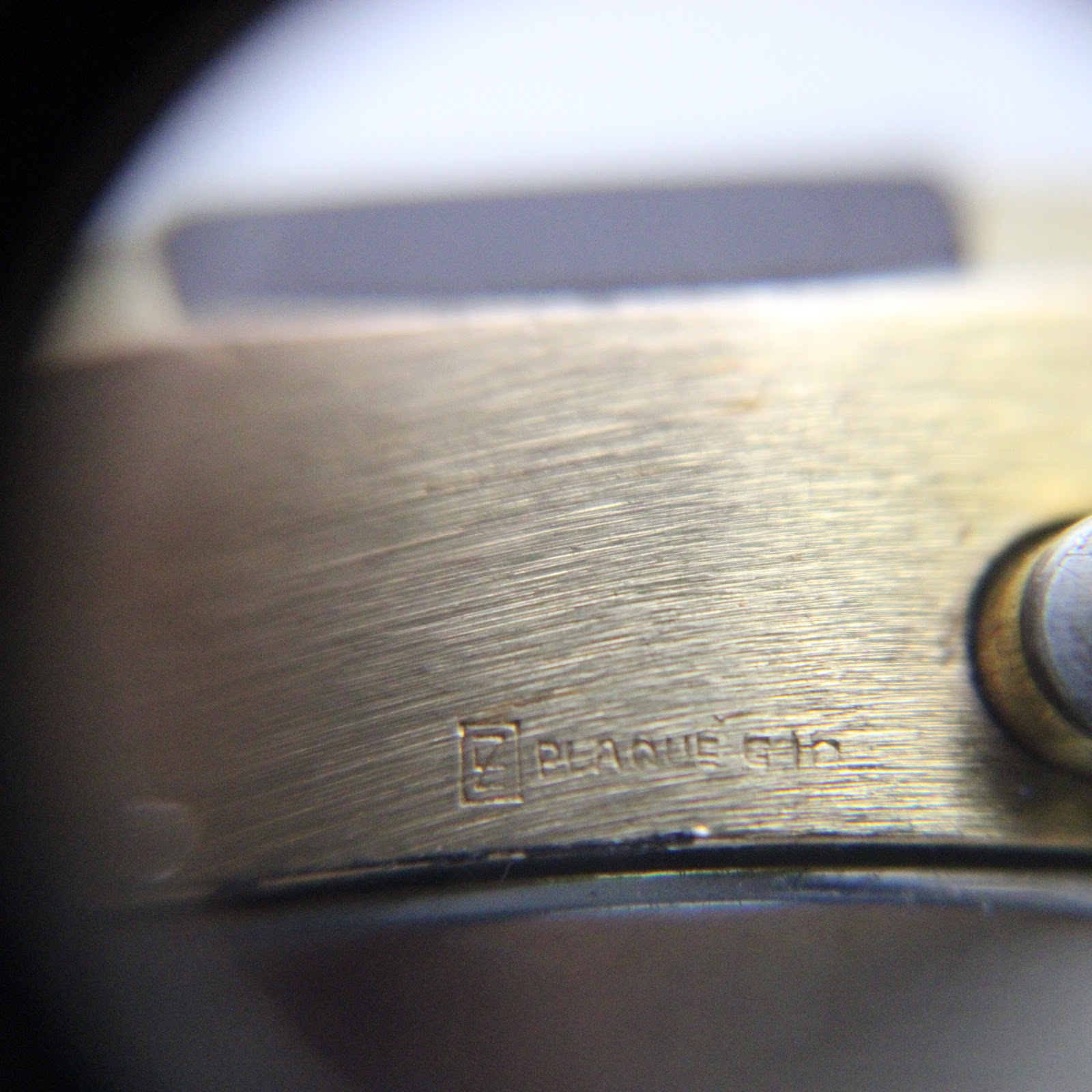 Close-up side view of the watch case, showing the 'PLAQUE G10' engraving which signifies gold plating, alongside the brushed finish.