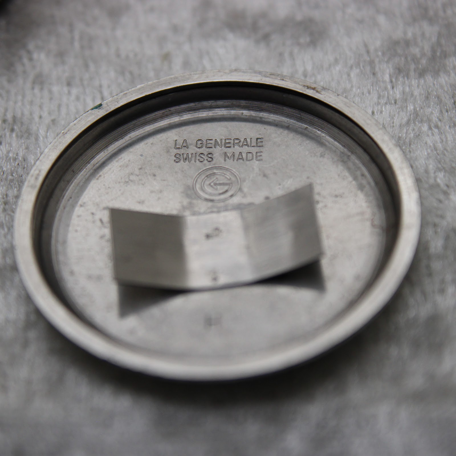 Close-up of the detached stainless steel case back, clearly engraved with 'LA GENERALE SWISS MADE' and the brand's arrow logo.