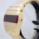 Side profile view of the watch case, showing the polished push-button crown for activating the display and a recessed setting pin, highlighting the gold plating.