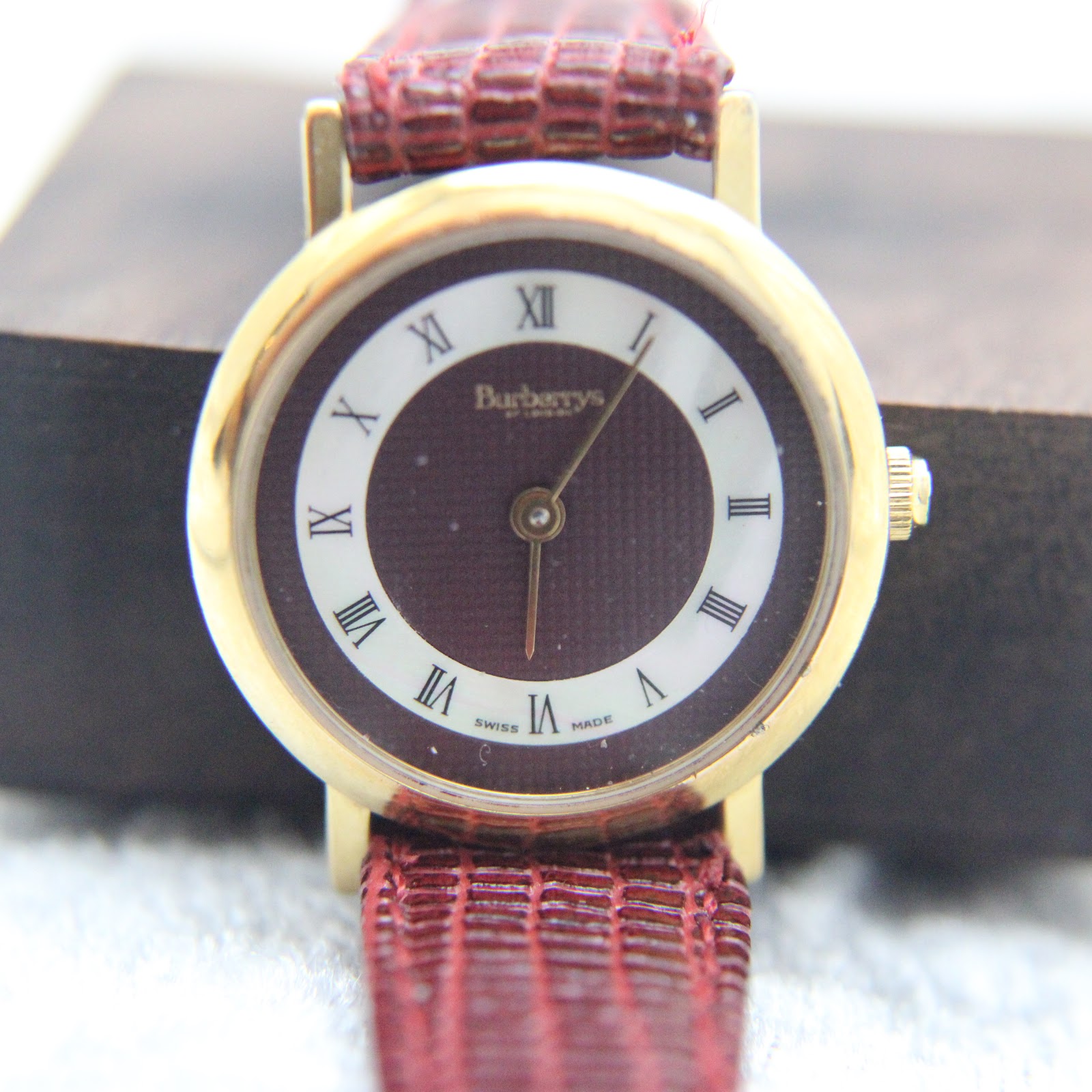 Front view of the Burberrys watch, positioned on a brown background, emphasising the dial details.