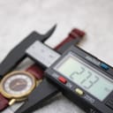 Digital caliper measuring the watch case diameter at 27.3mm, with the watch and strap visible.