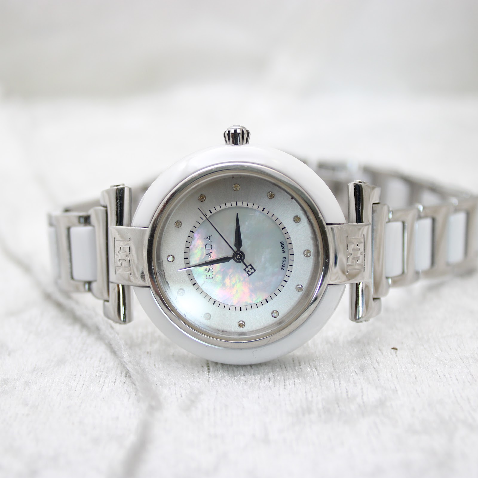 Front view of the Escada Lauren watch lying on a soft white fabric, displaying its polished and ceramic bracelet.