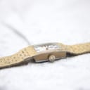 Side profile view of the Bulova watch and its integrated gold-plated bracelet on a light, textured surface.