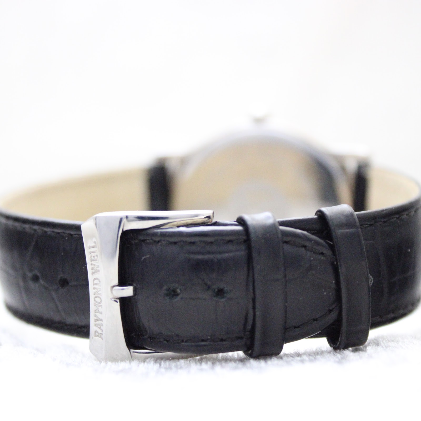 Close-up of the black leather strap with a signed Raymond Weil buckle.