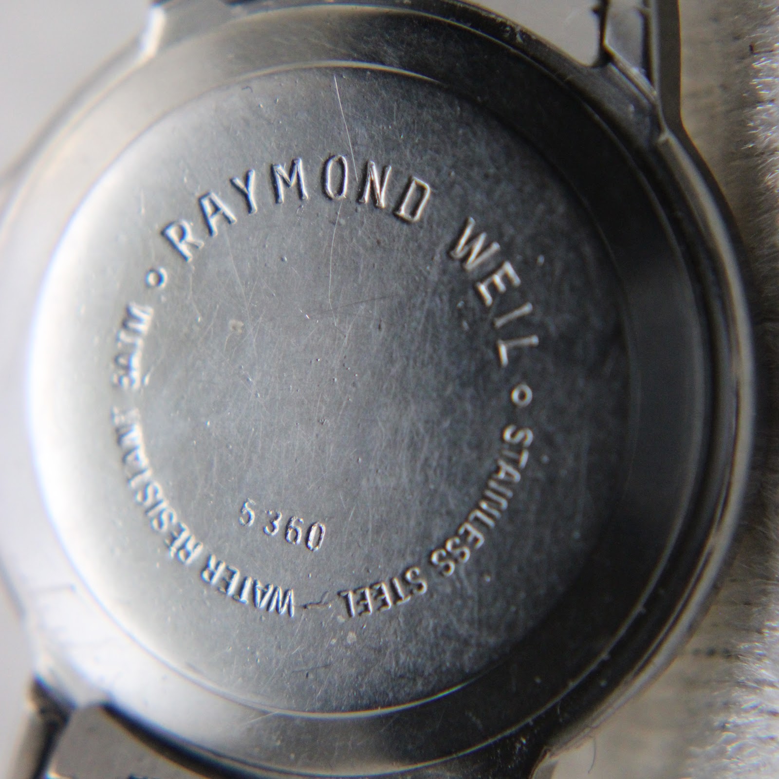 Close-up of the case back engraving "RAYMOND WEIL", "STAINLESS STEEL", "WATER RESISTANT 50M", and "5360".