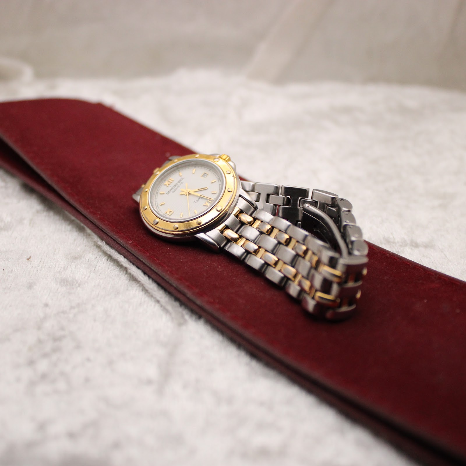 The Raymond Weil Tango watch resting on a red velvet presentation pouch.