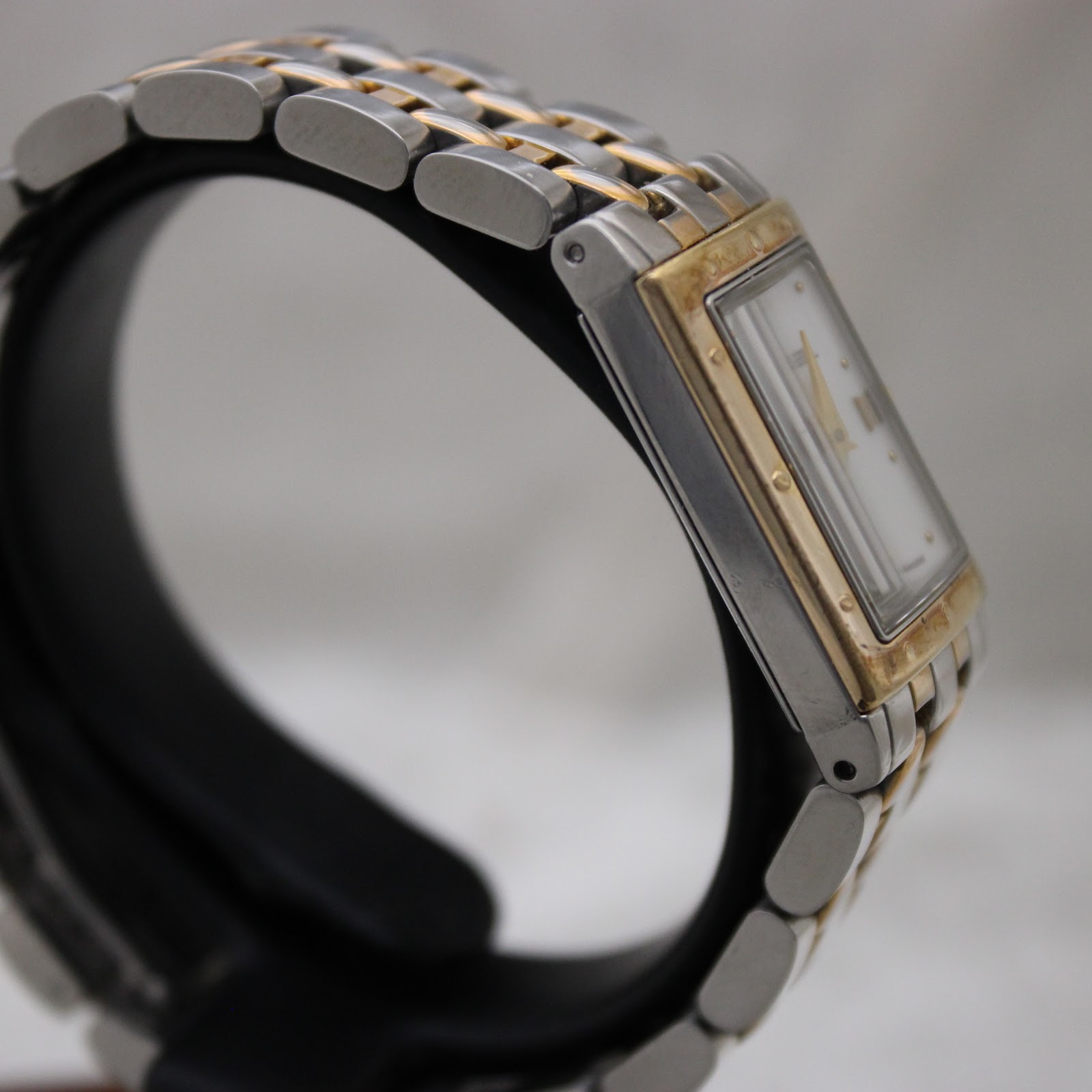 Left side profile view of the Raymond Weil Tango watch on a display stand, highlighting the rectangular stainless steel case and bi-tone bracelet.