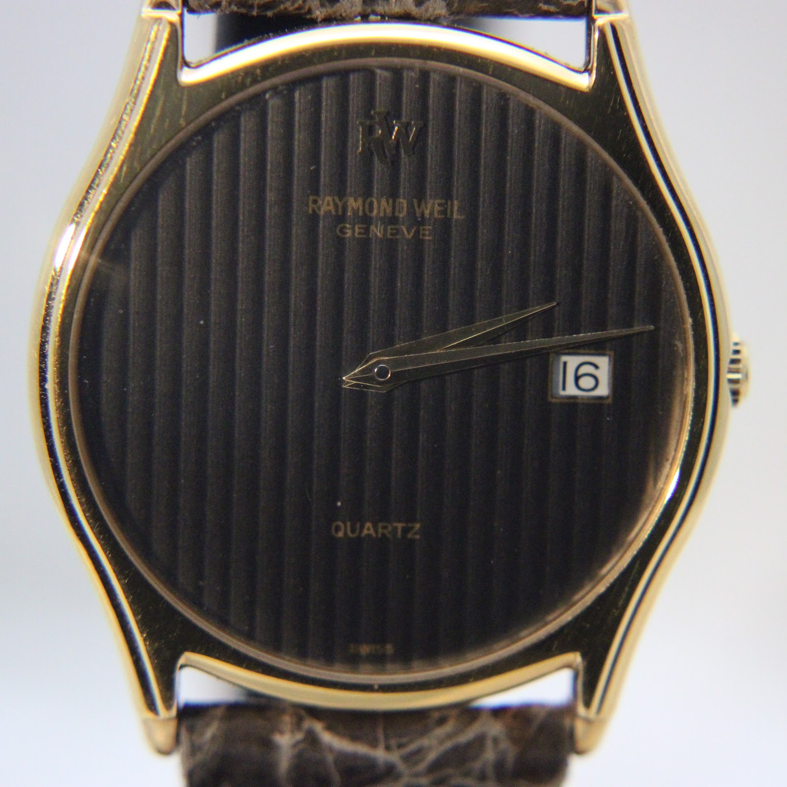 Close-up of the black vertical-striped dial, showing gold-tone hands, Raymond Weil Geneve branding, and the date display.