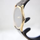 Side profile view highlighting the ultra-slim 18K gold electroplated case and original crown on a watch stand.