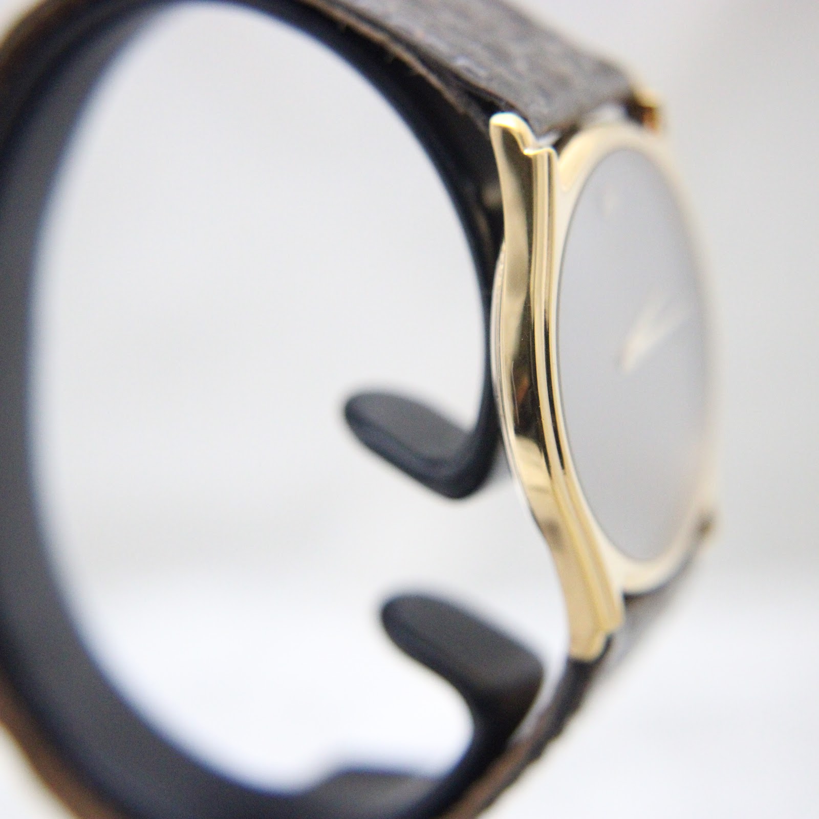 Angled side view demonstrating the slender profile and the elegant curve of the gold case with its dark brown leather strap.