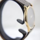 Angled side view demonstrating the slender profile and the elegant curve of the gold case with its dark brown leather strap.