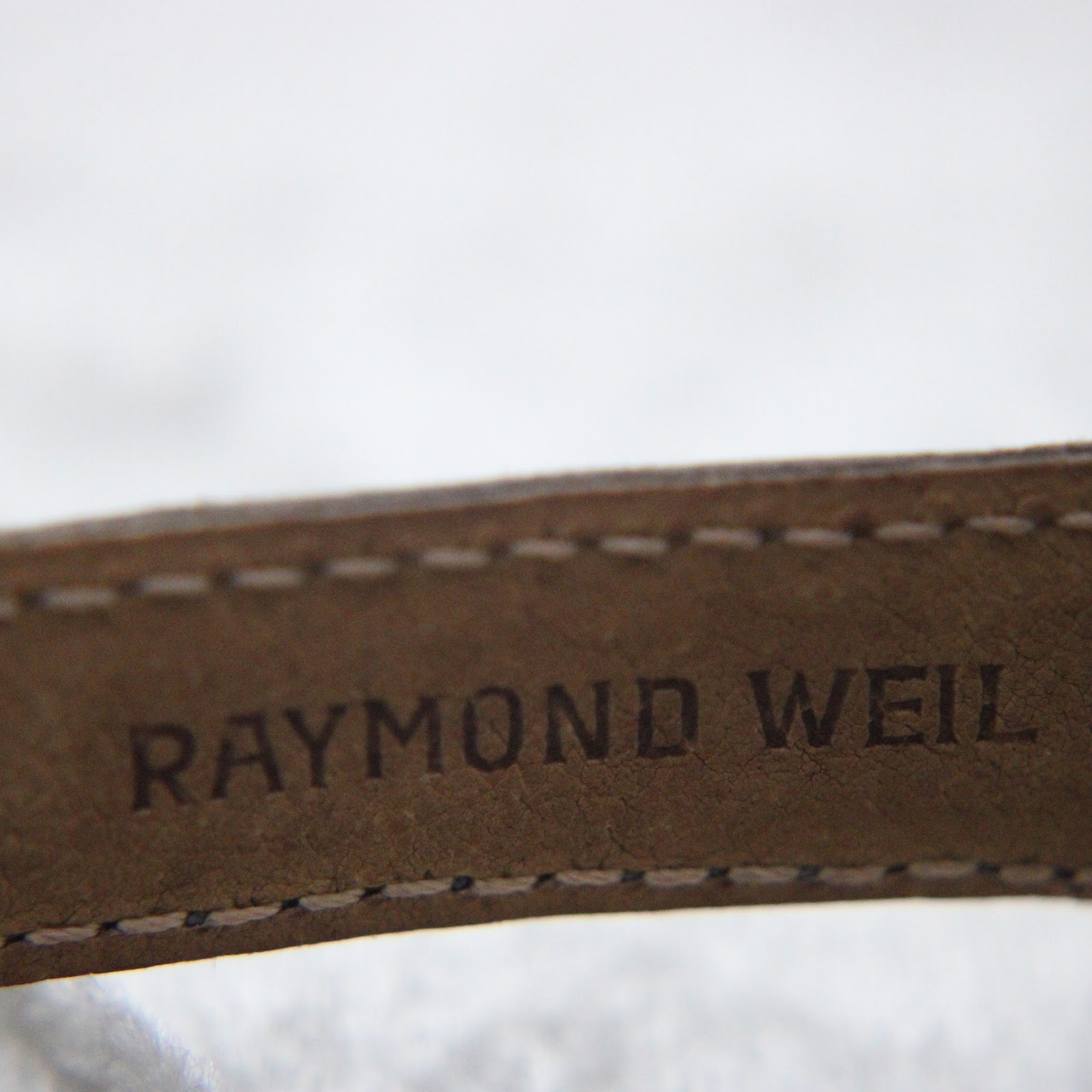 Close-up of the underside of the dark brown leather strap, revealing the embossed 'RAYMOND WEIL' branding.