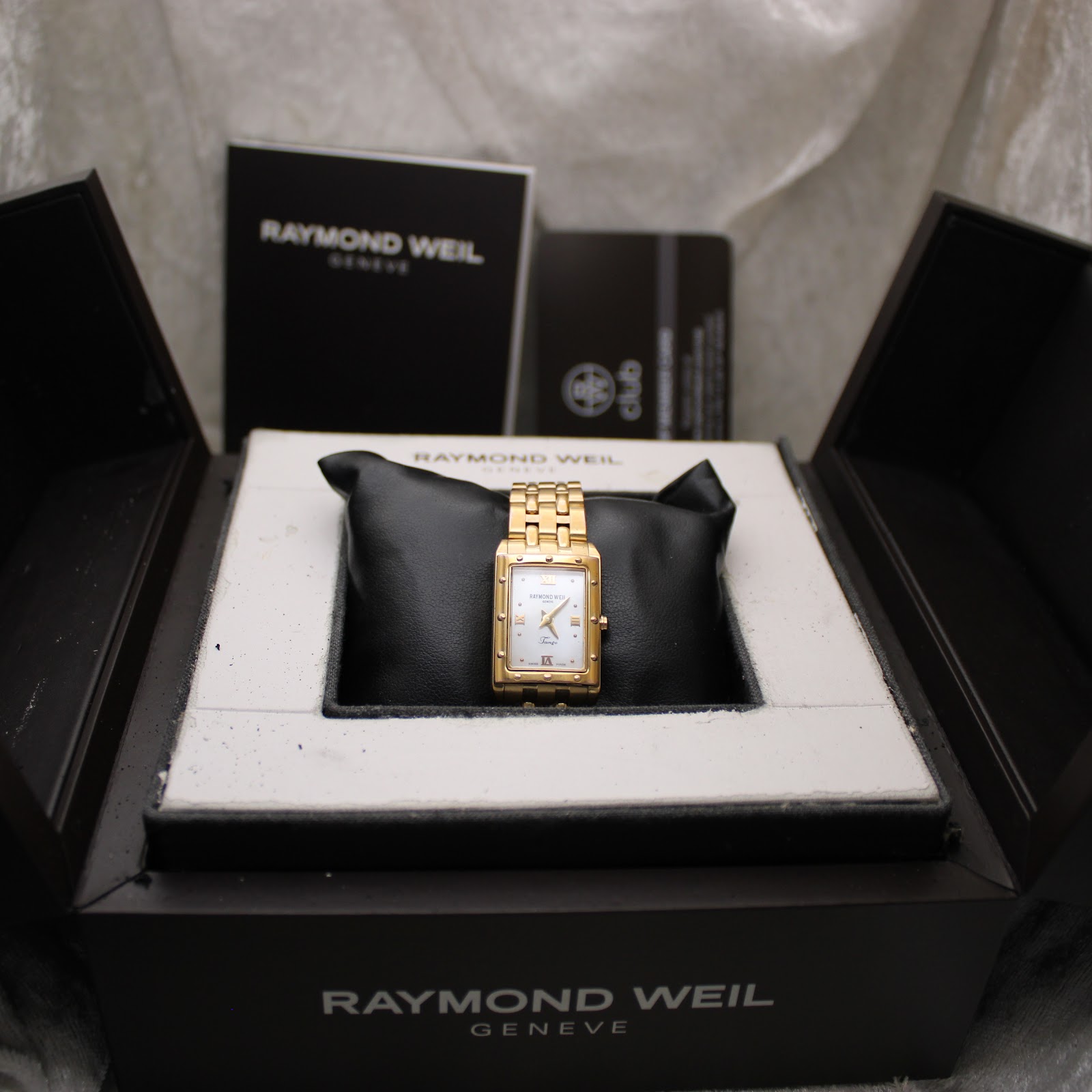 Raymond Weil Tango watch nestled in its original black presentation box, with manuals and documents in the background