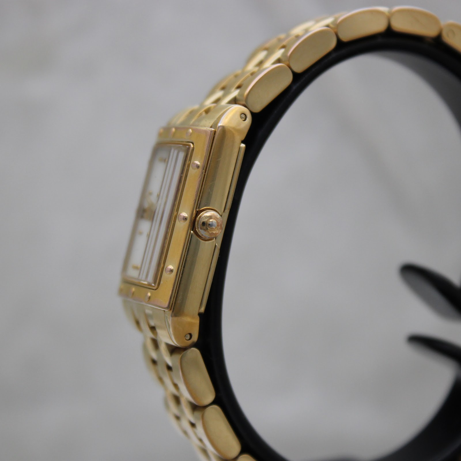 Side profile view of the gold Raymond Weil Tango watch case and link bracelet on a stand
