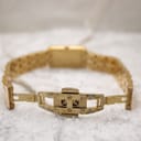 Close-up of the opened gold deployant clasp of the watch bracelet, showing 'stainless steel' inscription