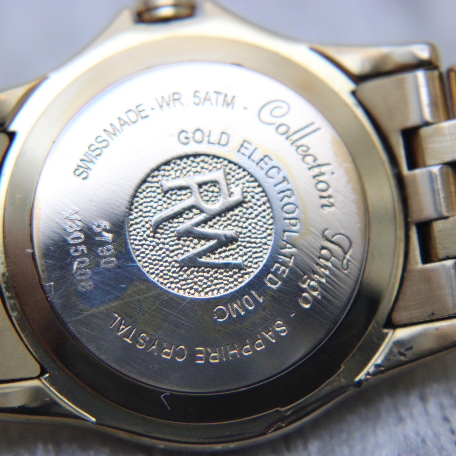 Close-up of the watch case back, detailing 'Swiss Made', 'WR. 5ATM', 'Gold Electroplated 10mc', 'Sapphire Crystal', 'Tango Collection', model '5790', and serial 'V305008'.