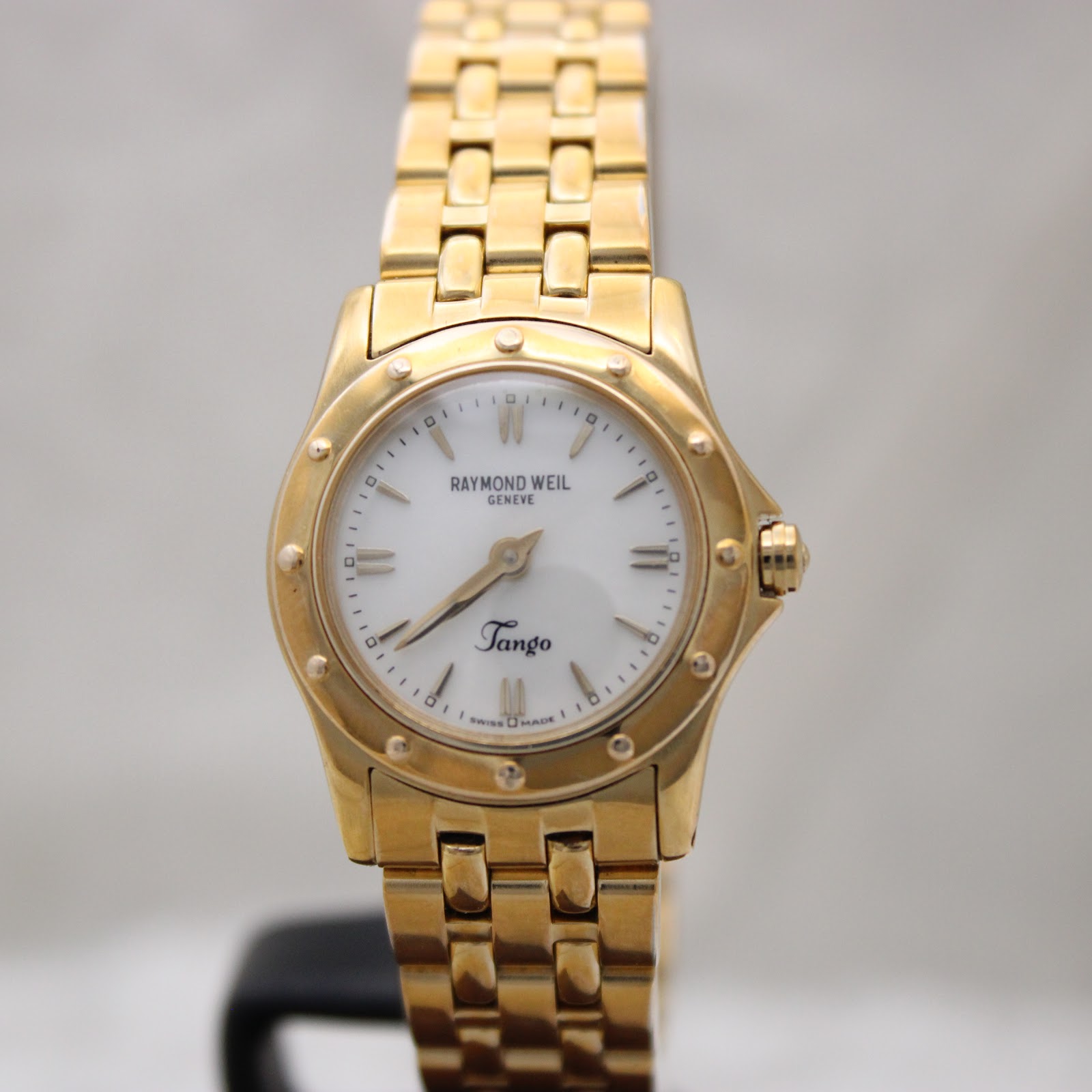 Angled front view of the Raymond Weil Tango watch dial and bracelet on a dark display stand.