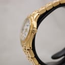 Side view of the watch, showing the gold electroplated case, fluted crown, and bracelet profile on a stand.