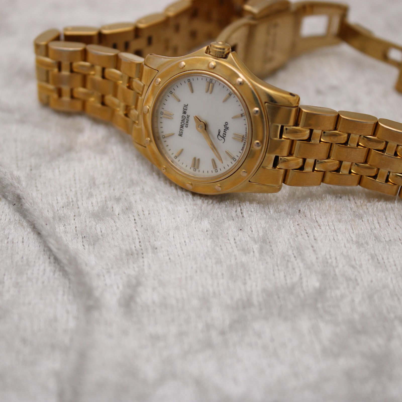 Overhead view of the Raymond Weil Tango watch resting on a light grey textured surface, displaying the full bracelet.