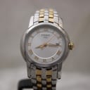 Close-up front view of the Tissot Ballade watch, highlighting the silver dial, gold Roman numerals, and date window.