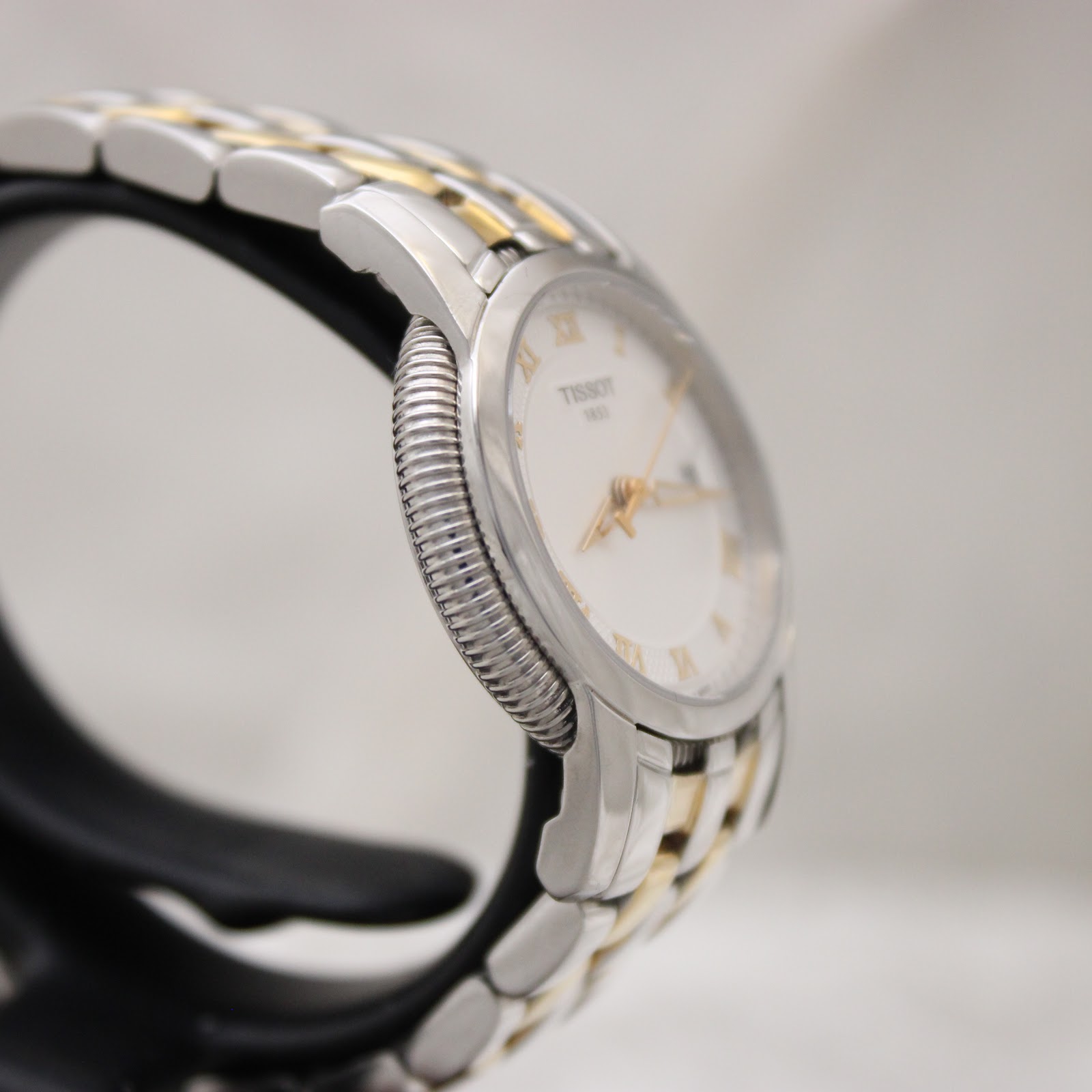 Side profile of the Tissot Ballade watch, showcasing the stainless steel case and gold-tone fluted bezel detail.