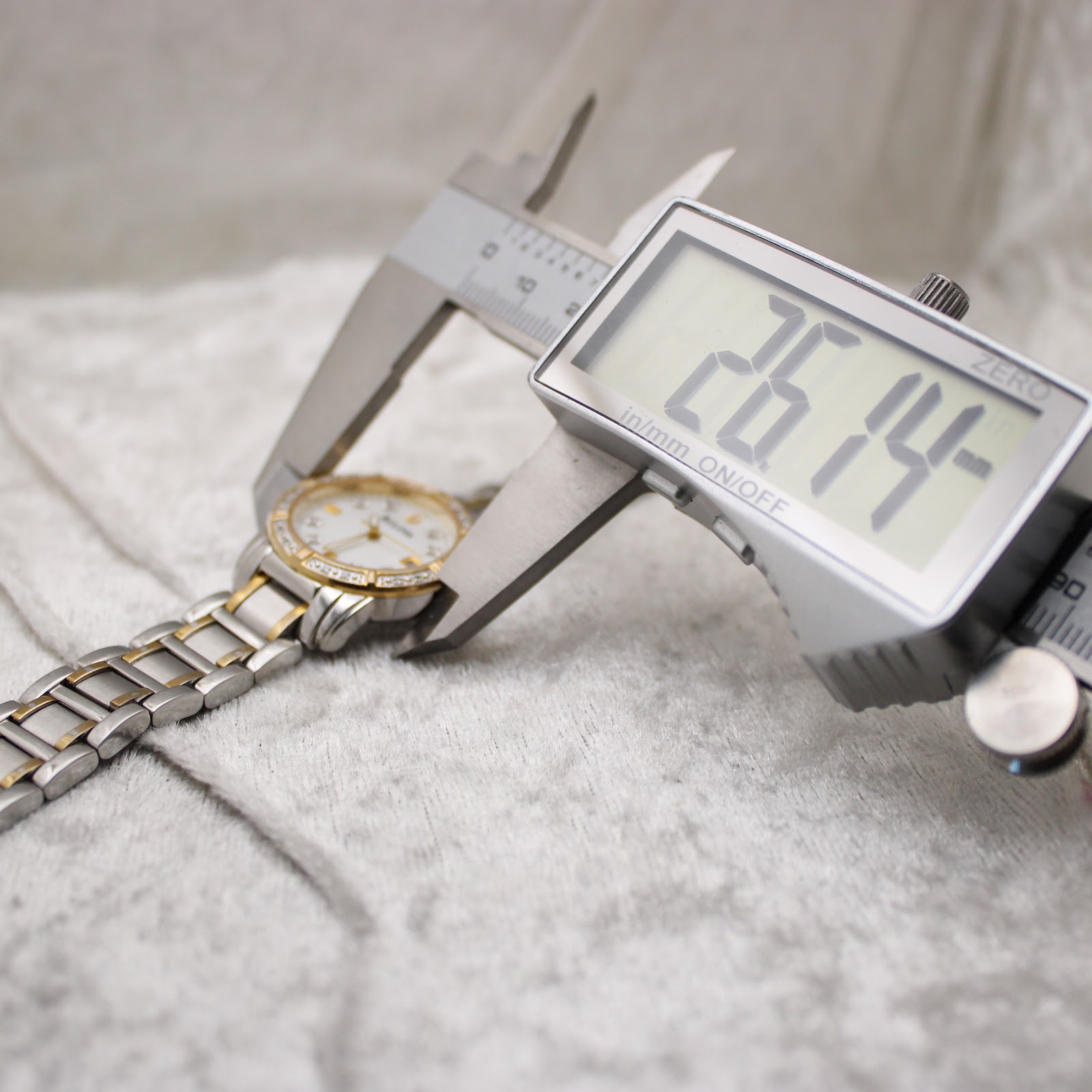 Digital caliper measuring the watch case diameter, displaying 26.14mm.
