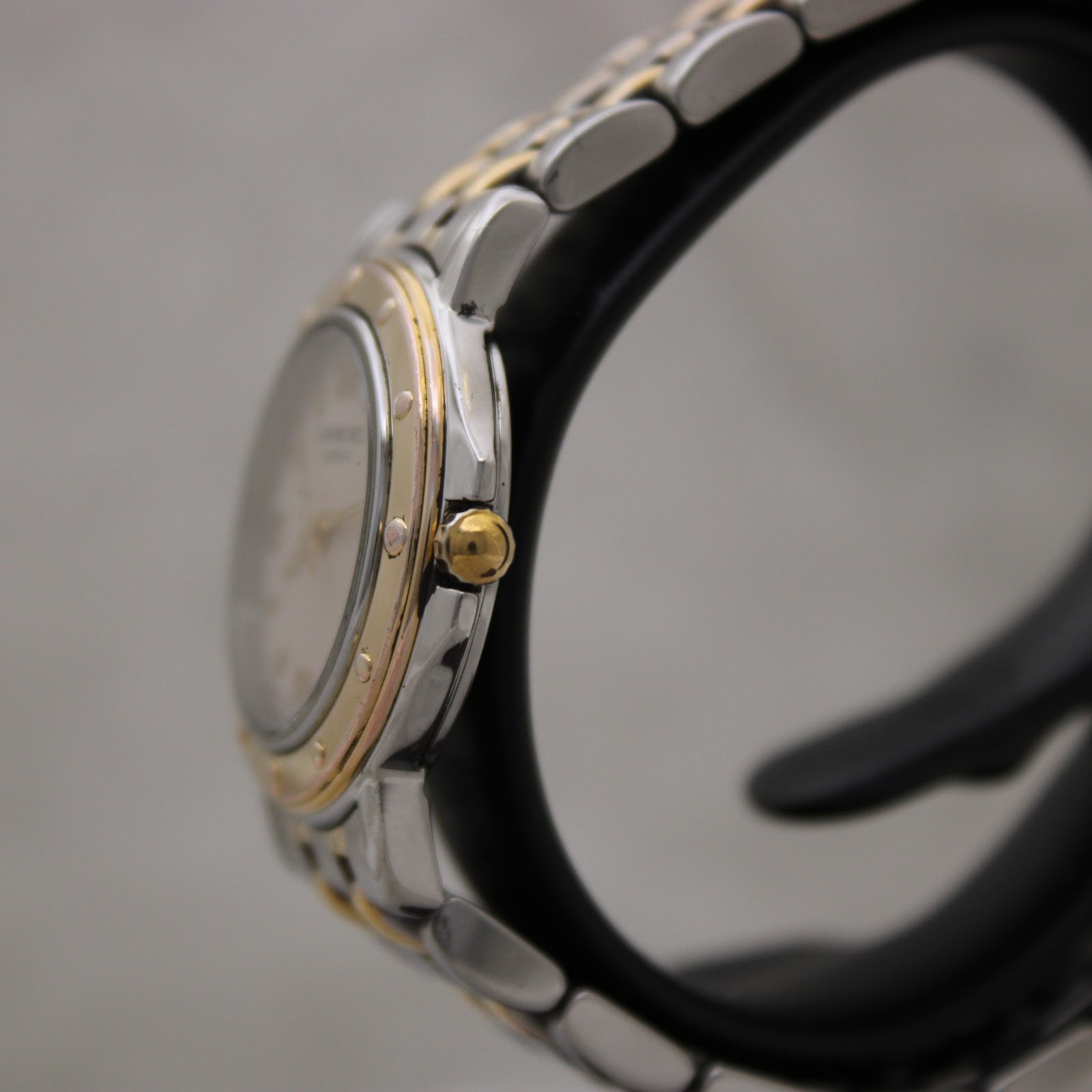 Side view of the Raymond Weil watch on a black stand, showing the gold-tone crown and the polished stainless steel case profile.