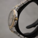 Side view of the Raymond Weil watch on a black stand, showing the gold-tone crown and the polished stainless steel case profile.