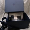 Overhead view of the Raymond Weil watch inside its original dark blue textured box with 'RW' logo, along with papers and cushion.