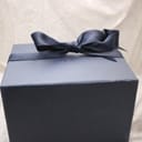 Close-up of the closed dark blue Raymond Weil watch box, tied with a matching blue ribbon.
