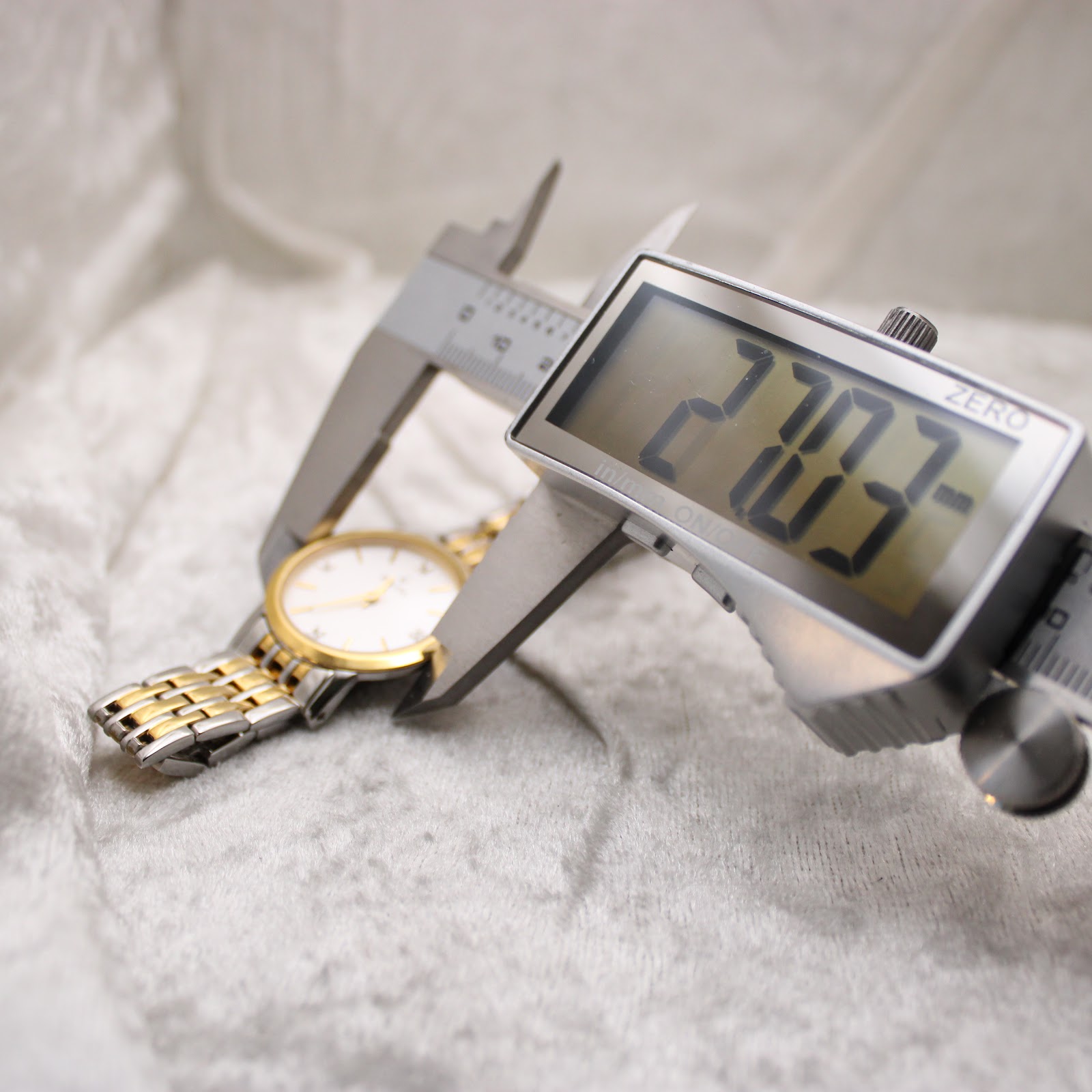 Digital caliper measuring the Bulova watch case diameter, displaying 27.70mm.