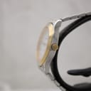 Side profile view of the Tissot PR 50, showing the gold-tone crown, bezel detail, and polished stainless steel case on a watch stand.