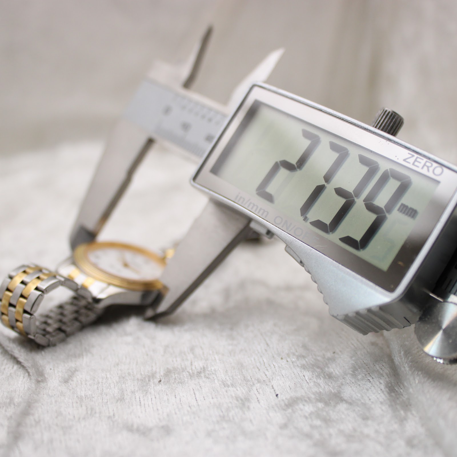 A digital caliper measuring the watch case, displaying an exact diameter of 27.39mm on a light background.