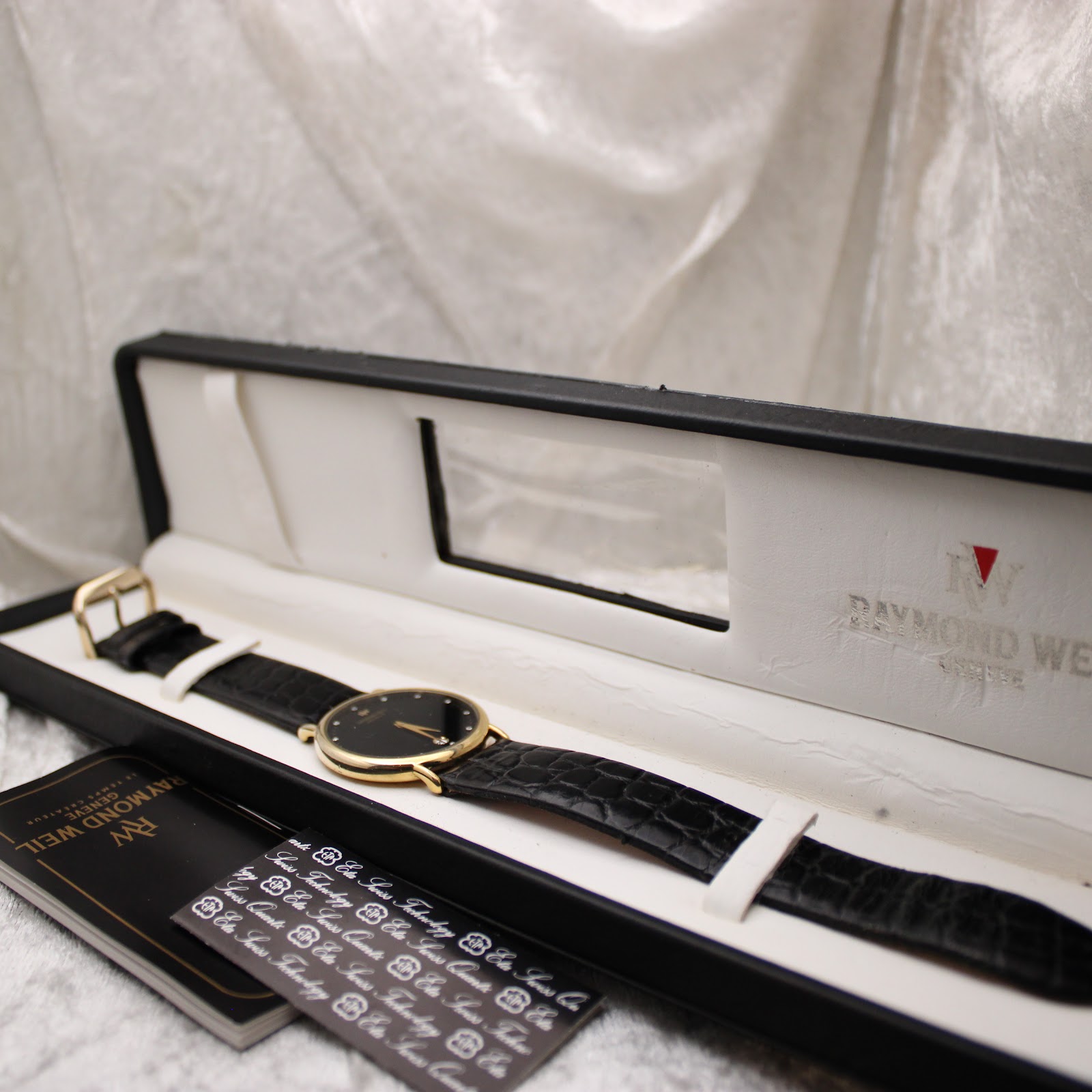 The Raymond Weil 9124 watch displayed within its original black presentation box, accompanied by the Raymond Weil booklet.