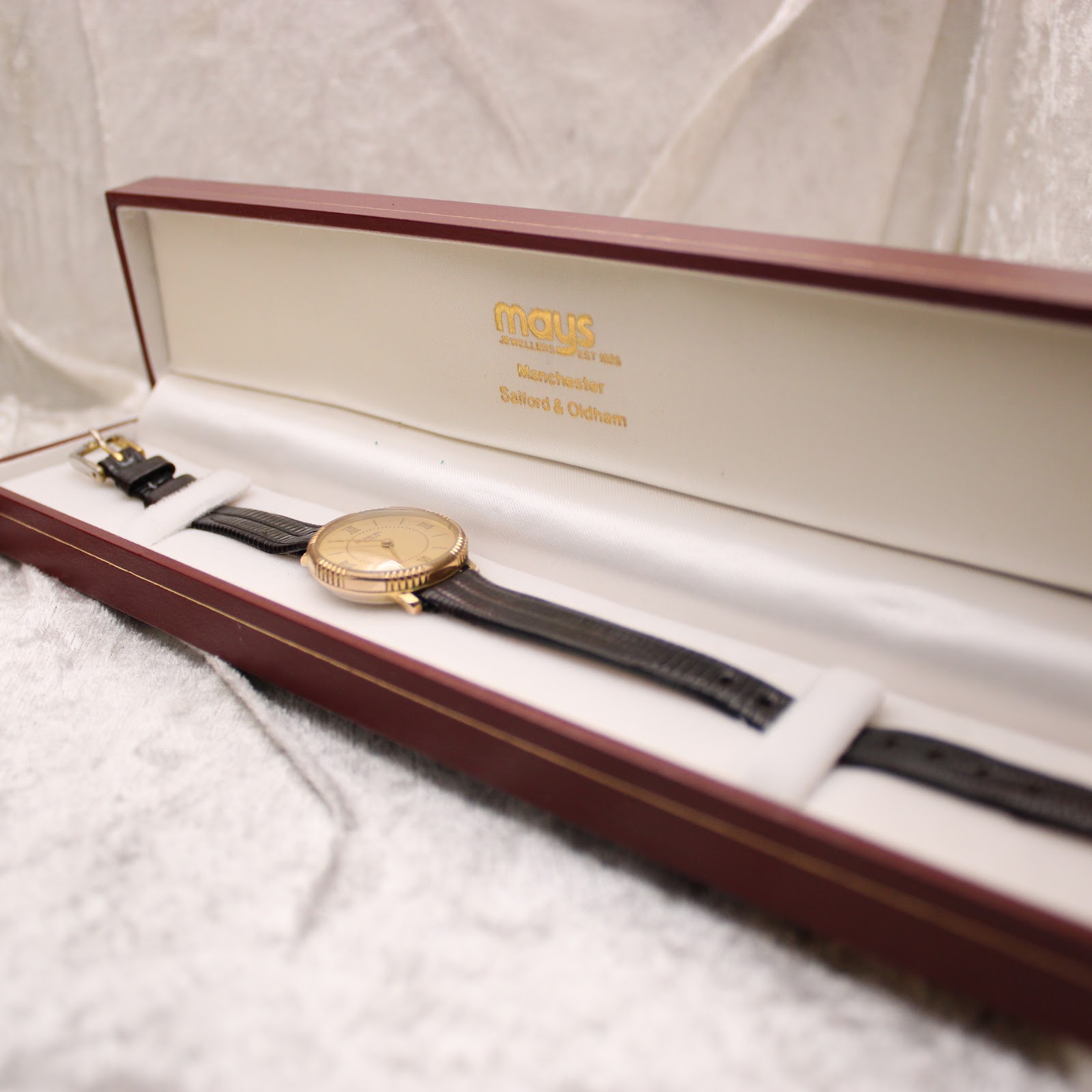 The Raymond Weil watch resting inside a dark red presentation box from "Mays Jewellers".