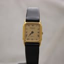 Front view of Raymond Weil Genève 5700 watch on a stand, showing rectangular gold electroplated case, champagne dial with Roman numerals, black hands, and black leather strap.