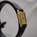 Another angled side view of the Raymond Weil Genève 5700 watch, focusing on the gold electroplated case and the minimalist design, set against a blurred background.