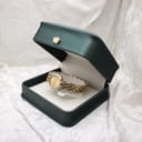The Raymond Weil watch nestled inside a dark green presentation box with a gold crown emblem.